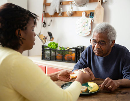 Man and women say at a table she is helping him with food.