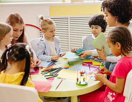 Two teachers and some children sat around a school desk